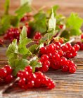 Fresh Redcurrants with green leaves on wooden surface — Stock Photo