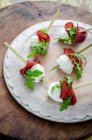 Buffalo mozzarella bites with bresaola and fresh rocket leaves canapes on a white wooden board and wooden background — Stock Photo