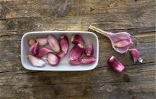 Spicchi d'aglio freschi in un piatto bianco su una superficie di legno — Foto stock