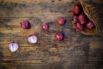 Cebollas rojas orgánicas en una cesta y delante de ella - foto de stock
