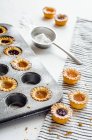 Mini albaricoques y tartaletas de mermelada de frambuesas en estaño y en la mesa con azúcar en polvo en tamizar - foto de stock