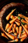 Сырая морковь в корзине с зелеными листьями в саду на черном фоне — стоковое фото