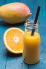 Un frullato di mango e arancia in bottiglia con una cannuccia — Foto stock