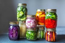 Gestapelte Einmachgläser mit frisch eingelegtem Gemüse vor grauem Hintergrund — Stockfoto