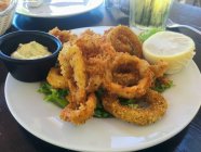 Жареные кольца кальмаров на белой тарелке с лимоном и соусом — стоковое фото
