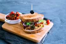 Un sándwich de pavo con pesto, brotes, aceitunas, tomates cherry y cebollas - foto de stock