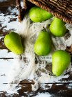 Green pears with cloth falling from basket on table — Stock Photo