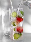 Acqua versata dalla bottiglia in vetro con cetriolo e fragole — Foto stock