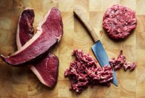 Bifes de carne, carne picada e um pedaço de carne com uma faca em uma tábua de cortar — Fotografia de Stock