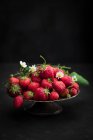 Strawberries with blossoms and green leaves in bowl — Stock Photo