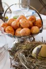 Ovos de cor marrom em um prato de prata atrás de um ovo de Páscoa pintado em um ninho de palha — Fotografia de Stock