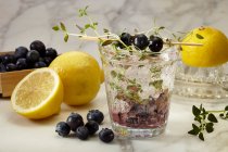 Verre de limonade aux myrtilles avec thym entouré d'ingrédients — Photo de stock