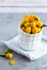 Kumquats em tigelas brancas empilhadas em pano e na superfície de concreto — Fotografia de Stock