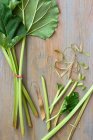 Rhubarbe, partiellement tranchée et entière avec de grandes feuilles sur une table en bois — Photo de stock
