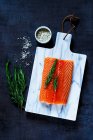 Filé de salmão cru fresco com alecrim e sal cinzento sobre tábua de corte em marbra — Fotografia de Stock