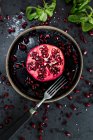 Half pomegranate and pomegranate seeds on plate and black surface with fork — Stock Photo