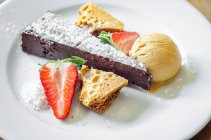 Pastel de chocolate y panal húmedo y rico servido con panal, helado y fresas frescas decoradas con azúcar glaseado - foto de stock