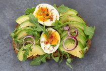 Bread topped with avocado, egg, rocket and red onion — Stock Photo
