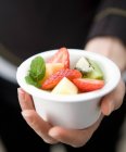 Main tenant une petite boule blanche avec salade de fruits mélangés — Photo de stock
