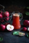 Fresh apple juice in jug and whole crimson Cousinot apples — Stock Photo