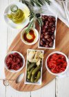 Antipasto prato - tomates secos ao sol e capsicum, azeitonas kalamata, pepinos, alcachofras, pães, azeite (com vinagre balsâmico) e ramo de oliveira — Fotografia de Stock
