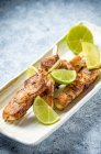 Grilled chicken breast skewers with lime on a light plate and light travertine marble table — Stock Photo