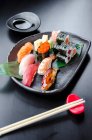 Bandeja de sushi mista fresca japonesa com salmão, atum, cauda amarela, camarão nigiri, maki de salmão, maki de atum em um prato preto e mesa preta — Fotografia de Stock