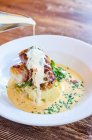 Sea bass fish fillets wrapped in bacon on a potato mash with spinach and chives with a pour of white wine sauce — Stock Photo