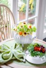 Bouquet di foglie di insalata e fiori a base di formaggio, carote e avocado in una teiera, crescione e carote in una tazza di tè su un tavolo verde — Foto stock