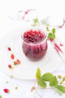 Mermelada de fresas silvestres caseras en frasco de vidrio con bayas frescas y hojas en el plato - foto de stock
