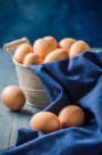 Fresh eggs in rustic metal basket and blue cloth — Stock Photo