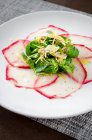 Carpaccio di tonno fresco con insalata di erbe e carciofi conditi con olio d'oliva su un piatto bianco — Foto stock