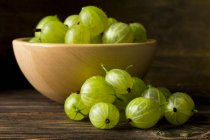 Green gooseberries in wooden bowl and on table surface — Stock Photo