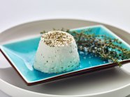Formaggio di capra fresco con erbe aromatiche su un piatto blu — Foto stock
