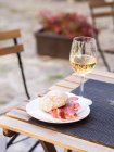 A ham sandwich and a glass of white wine on a bistro table outdoors — Stock Photo