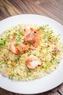 Sicilian pistachio and king prawns risotto with herbs on a white plate and a wooden background — Stock Photo