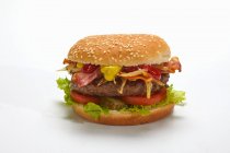 Um hambúrguer com bacon e queijo contra uma superfície branca — Fotografia de Stock