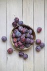 A dish of ripe plums against a white wood background — Stock Photo