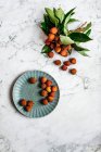 Frische Litschis auf Teller und Marmoroberfläche mit grünen Blättern — Stockfoto