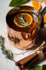 Apple cider heated in an antique copper pot, with oranges with leaves, orange slices, cinnamon sticks and sugared rosemary — Stock Photo