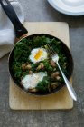 Kale with mushrooms and fried eggs in pan with fork — Stock Photo
