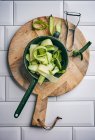 Legumes verdes frescos na placa de corte de madeira com faca e garfo na mesa da cozinha — Fotografia de Stock