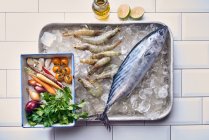 Bonito and tiger prawns on ice next to fresh vegetables and herbs — Stock Photo