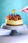 Bolo de queijo com figos e mel e mão segurando pau com mel pingando — Fotografia de Stock
