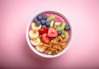 Summer acai smoothie bowl with strawberries, banana, blueberries, kiwi fruit and granola on pastel pink background — Stock Photo