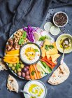 Meze platter with hummus, yoghurt dip, assorted snacks: Hummus in bowl, vegetables sticks, chickpeas, olives, pita, chips — Stock Photo