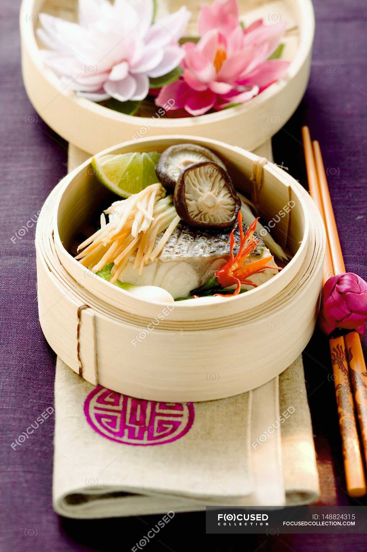 Steamed sea bass with ginger and vegetables in wooden bowl over towel ...