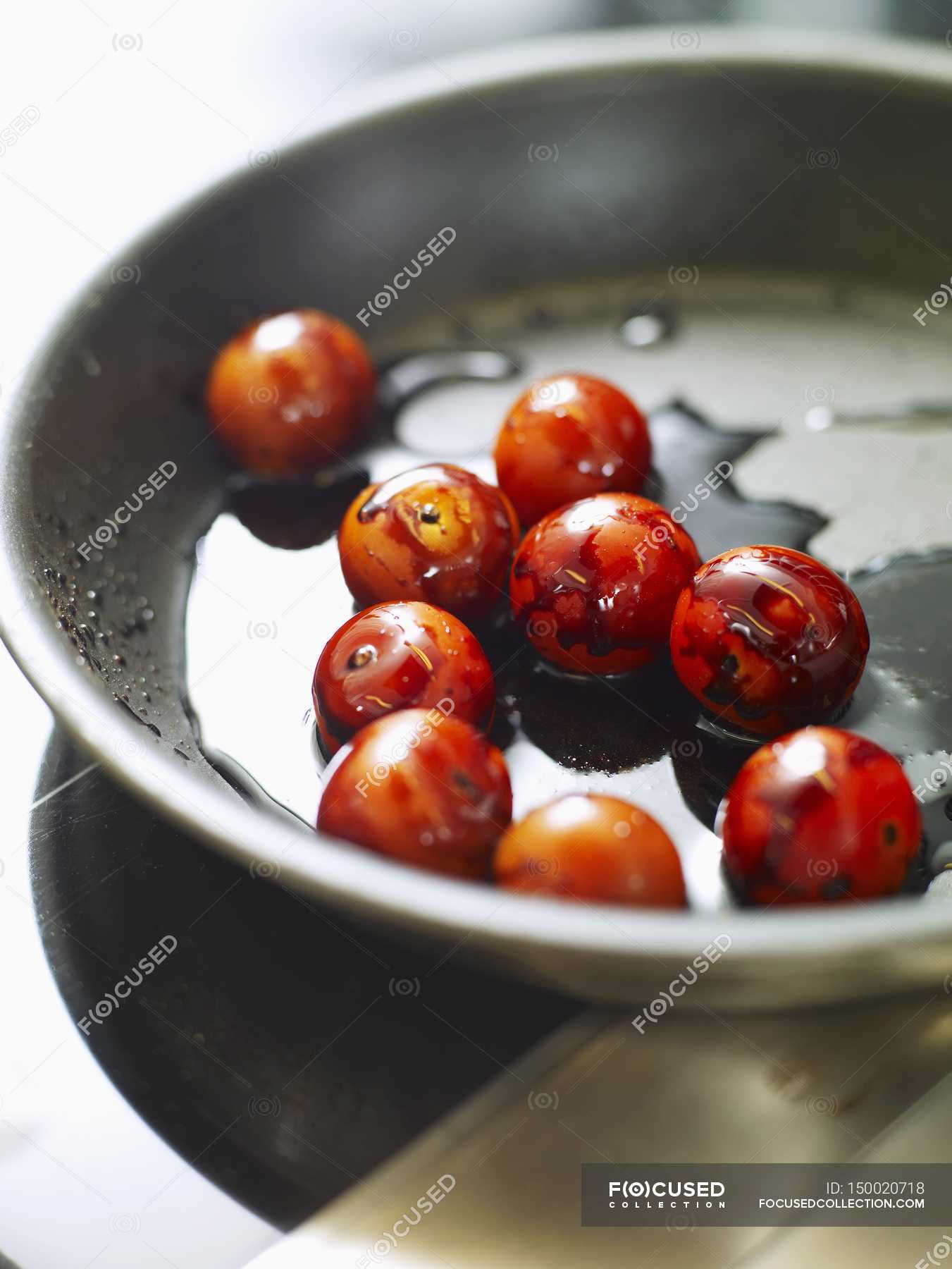 Frying cocktail tomatoes with balsamic vinegar in frying pan — close