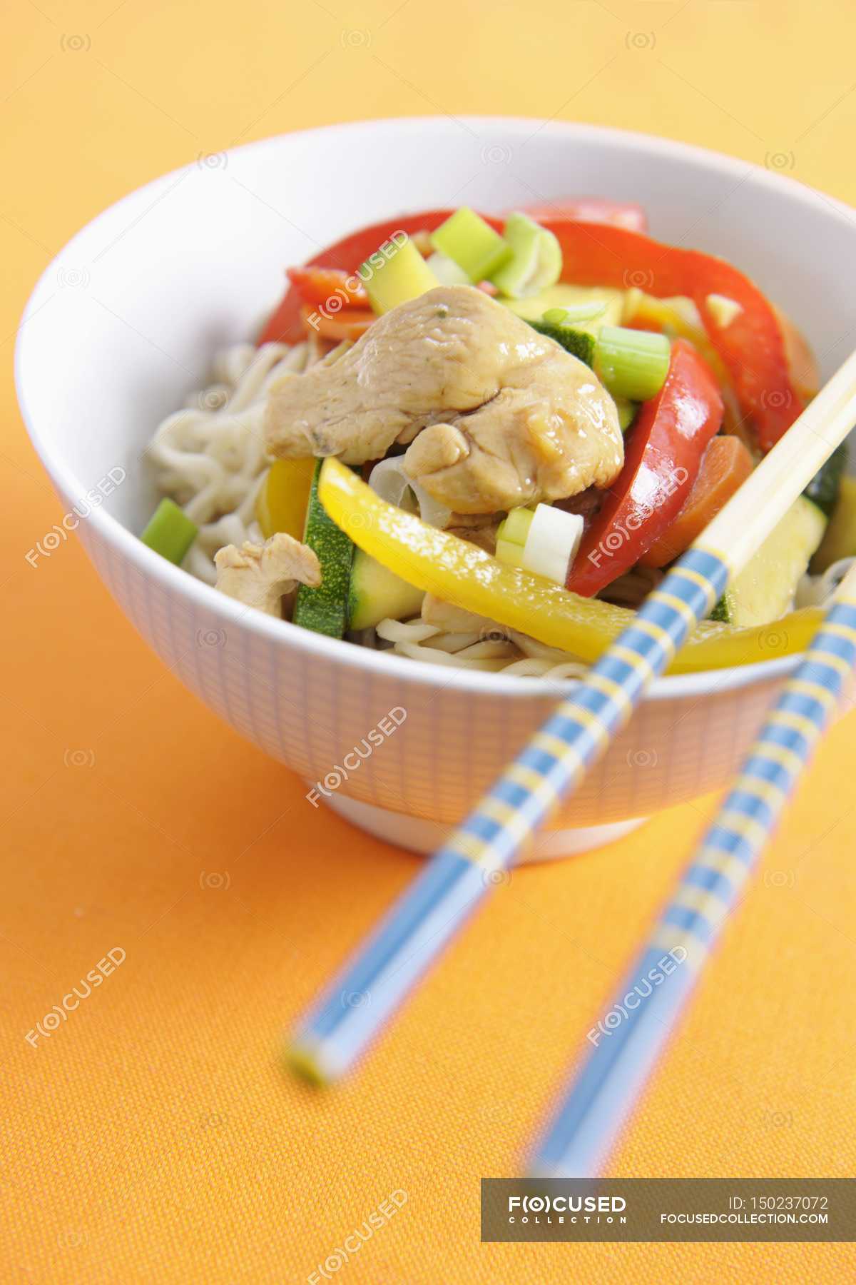 Stirfried chicken and vegetables on noodles on white plate over orange