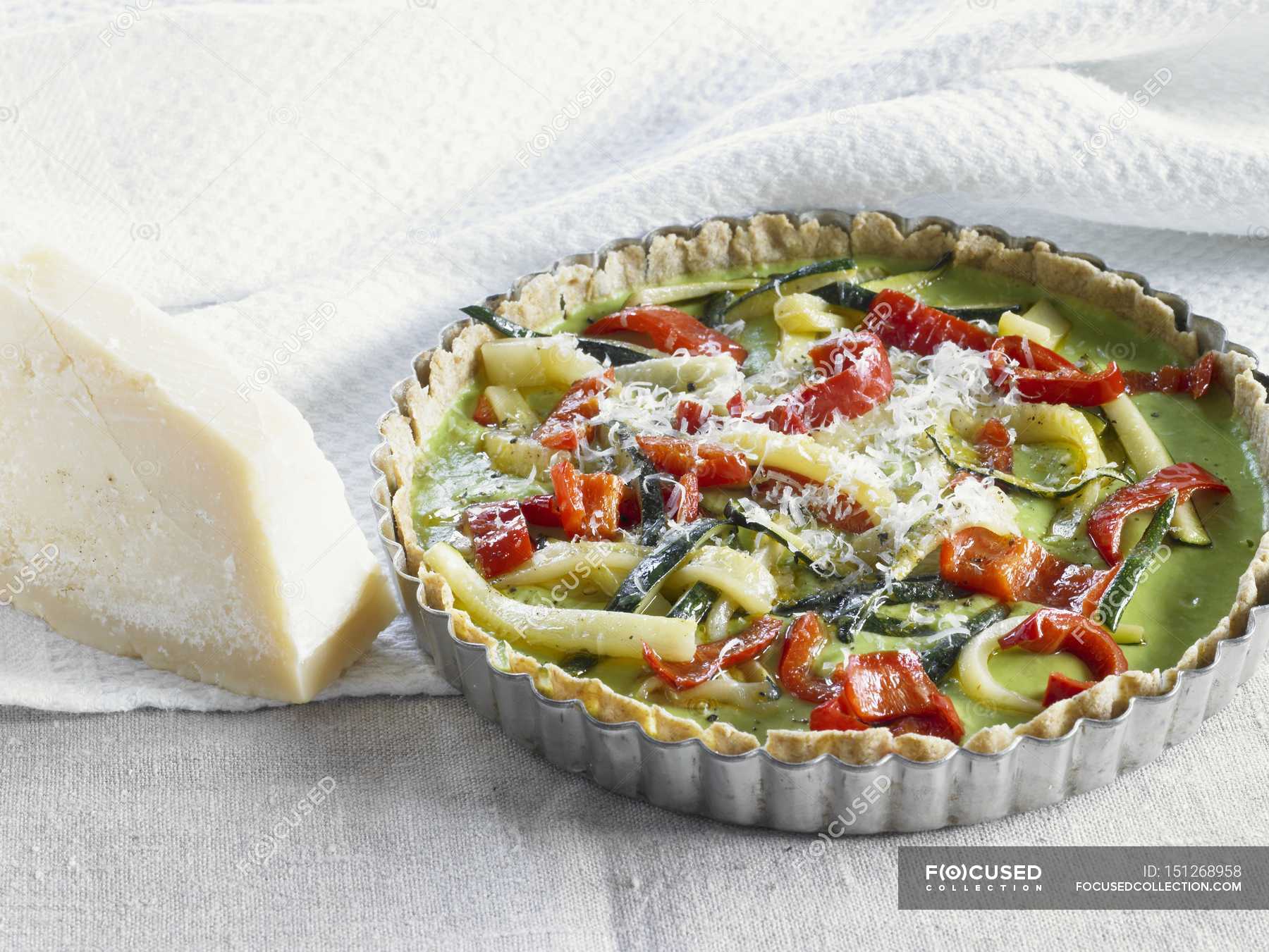 Courgette and pepper quiche in a dish over wooden surface with towel